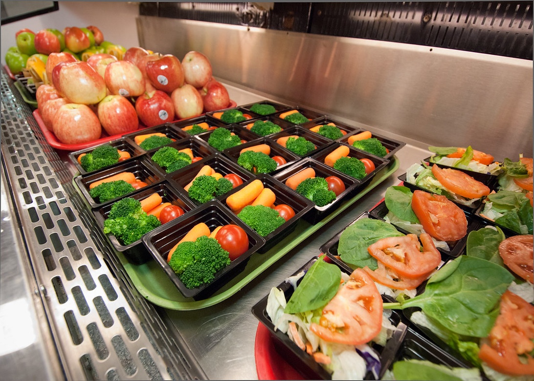 En moderne skolekantine præsenterer et indbydende udvalg af sunde frokostkomponenter, herunder friske grøntsager og frugt.