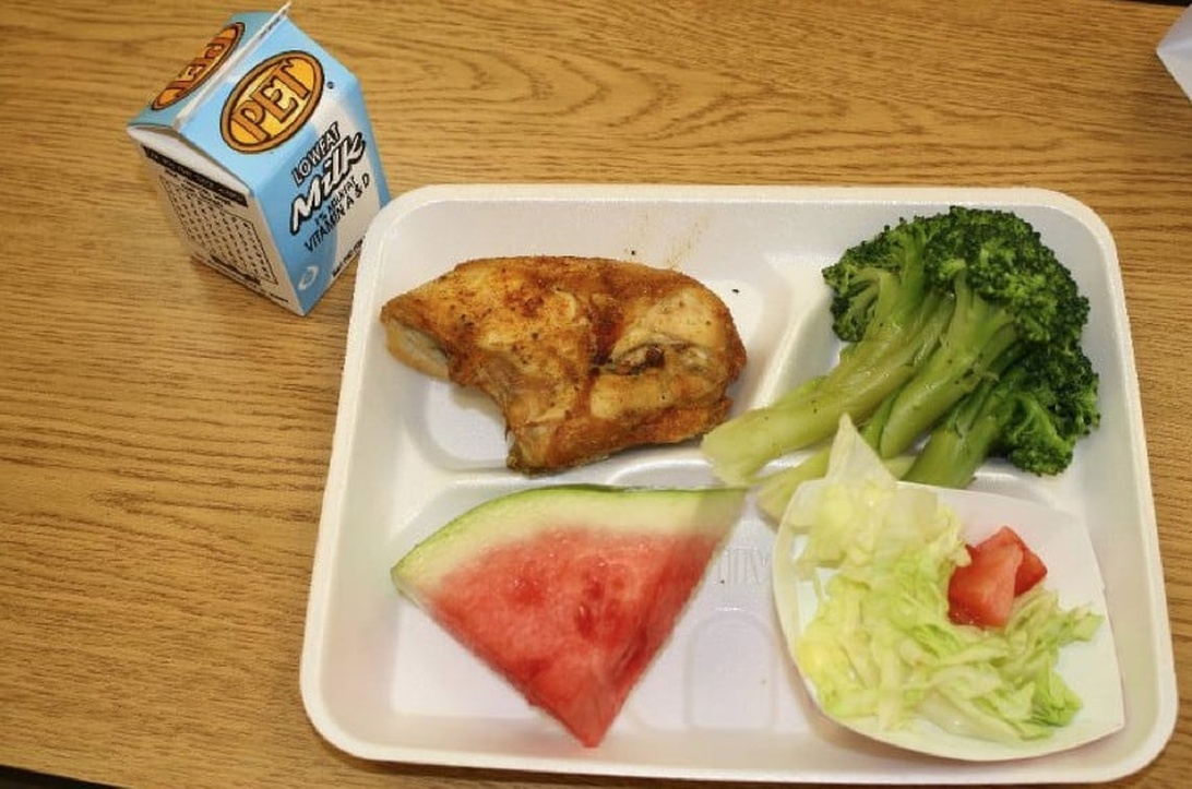 En velafbalanceret og nærende skolefrokost serveret på en bakke, med kylling, broccoli, vandmelon, salat og mælk.